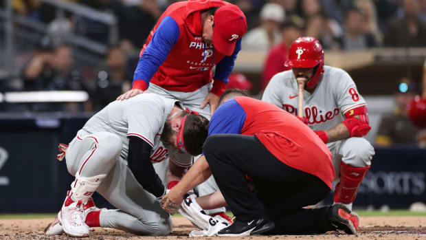Philadelphia Phillies’ Bryce Harper, left, receives attention after being hit by a pitch while interim manager Rob Thomson, background left, and Nick Castellanos, background right, look on during the fourth inning of the team’s baseball game against the San Diego Padres, Saturday, June 25, 2022, in San Diego. (AP Photo/Derrick Tuskan)